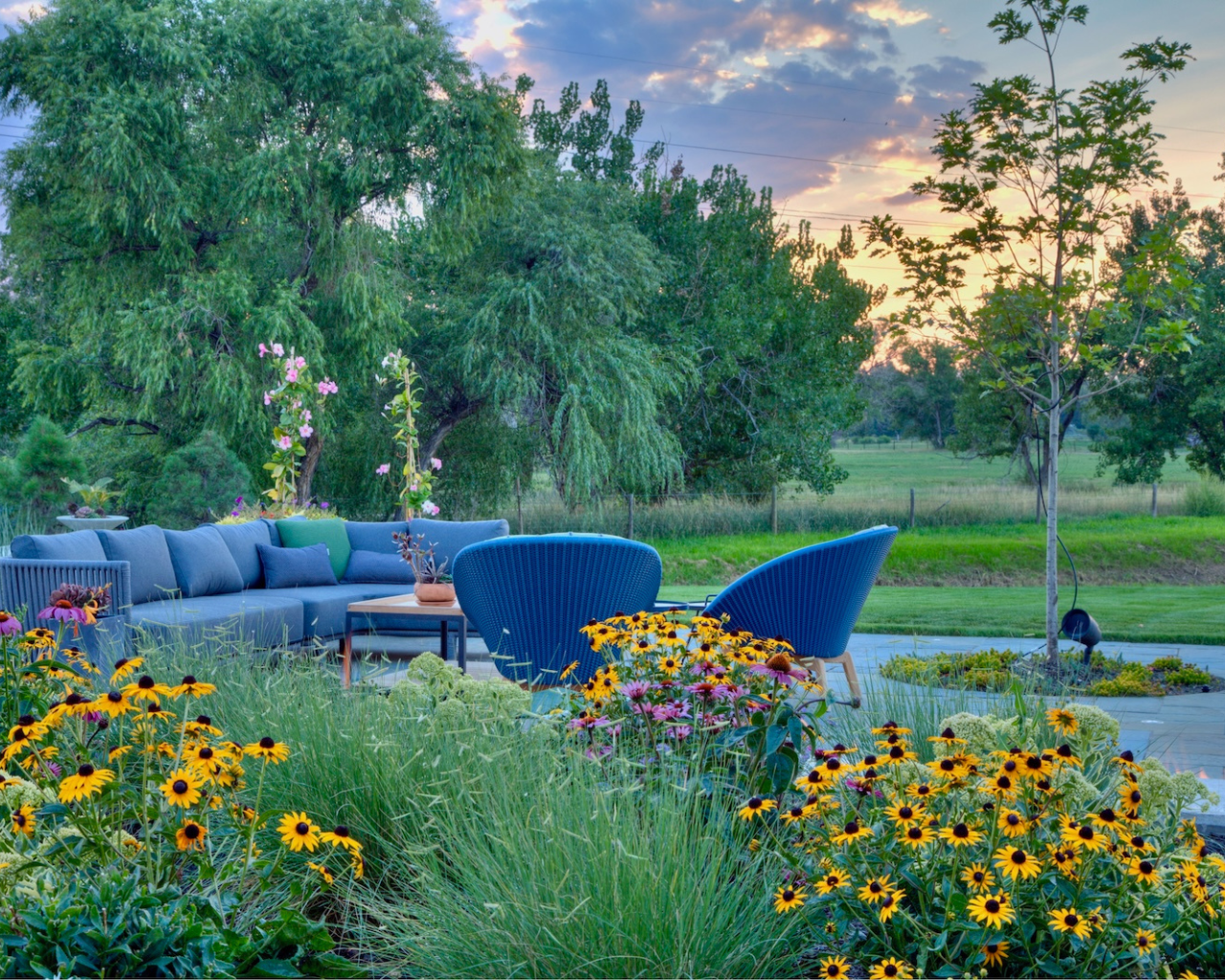 Outdoor seating with blue chairs among colorful flowers under a sunset sky, inspired by The Scout Guide.